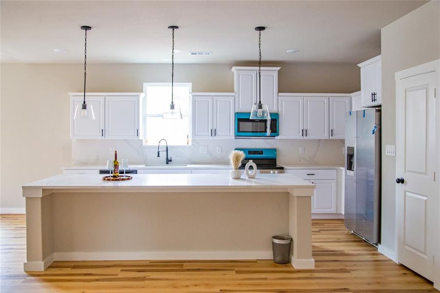 Kitchen with white cabinetry, appliances with stainless steel finishes, a center island, decorative light fixtures, and light wood-style flooring