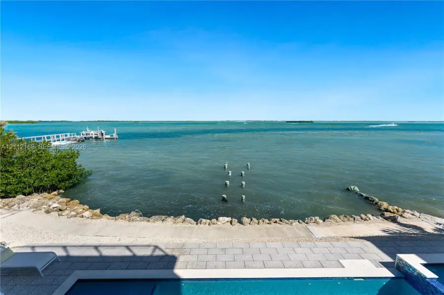 Waterfront property featuring a private swimming pool, stone-paver patio, rock-lined seawall, and a private dock Waterfront property featuring a private swimming pool, stone-paver patio, rock-lined seawall, and a private dock