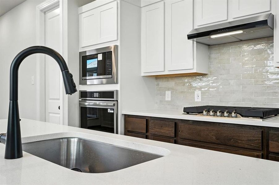 Kitchen with backsplash, appliances with stainless steel finishes, under cabinet range hood, white cabinetry, and light stone counters Kitchen with backsplash, appliances with stainless steel finishes, under cabinet range hood, white cabinetry, and light stone counters