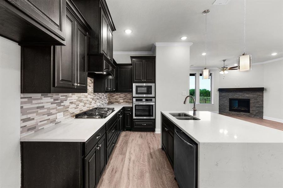 Kitchen featuring ceiling fan, dark cabinetry, light wood finished floors, tasteful backsplash, and crown molding Kitchen featuring ceiling fan, dark cabinetry, light wood finished floors, tasteful backsplash, and crown molding