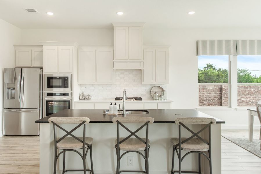 Kitchen with white cabinets, stainless steel appliances, and island with three bar stools Kitchen with white cabinets, stainless steel appliances, and island with three bar stools