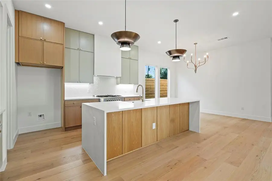 Kitchen with backsplash, modern cabinets, light stone counters, hanging light fixtures, and light wood-style flooring