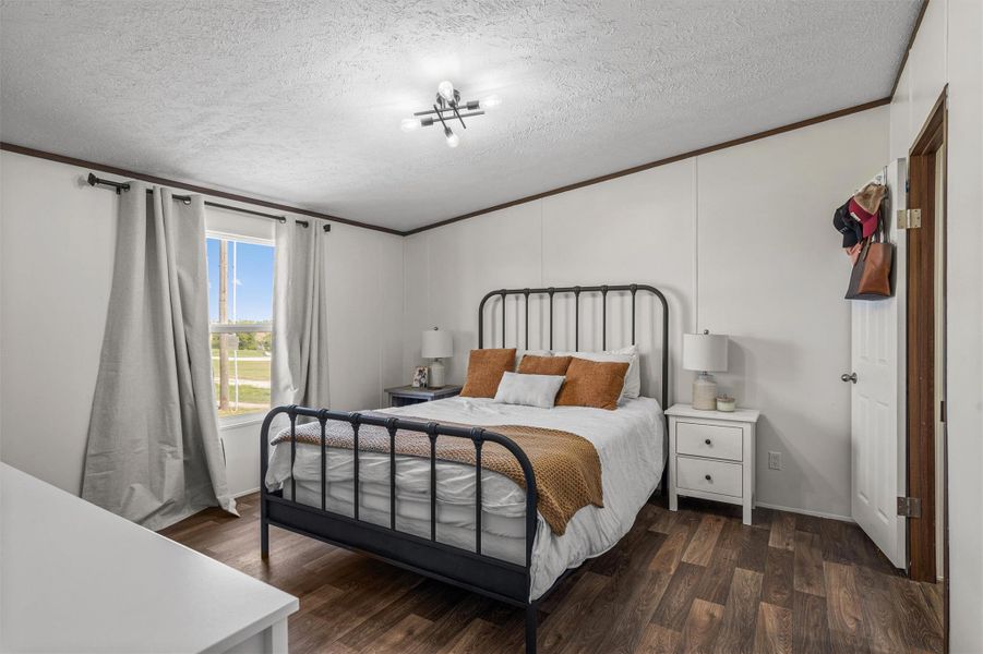 Bedroom with dark wood-type flooring, ornamental molding, and a textured ceiling