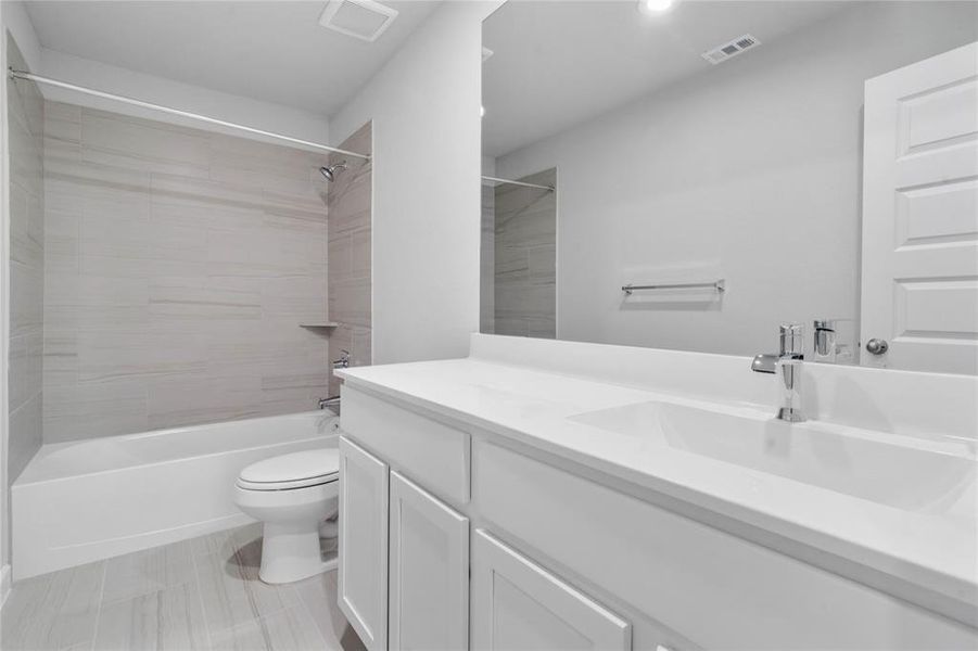 Secondary bath features tile flooring, bath/shower combo with tile surround, stained cabinets, beautiful light countertops, mirror, sleek fixtures and modern finishes.