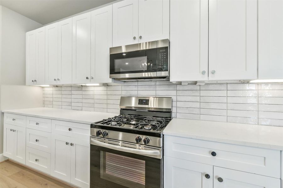 Kitchen features stainless steel gas range, built-in microwave and ample cabinet space with a modern tile backsplash.