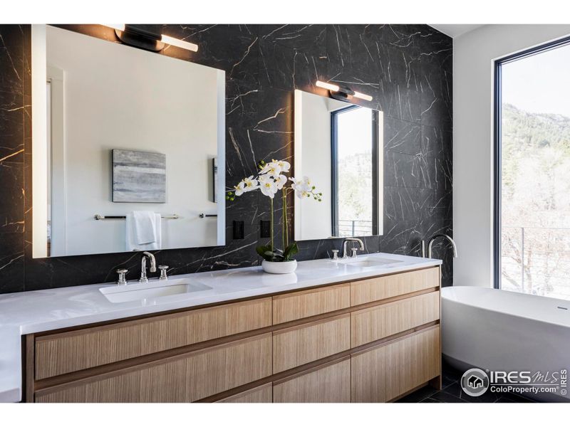 The primary bathroom offers its own spa-like retreat with a soaking tub looking out to the foothills, custom white oak cabinetry, quartz countertops, lighted mirrors and sleek tile work.