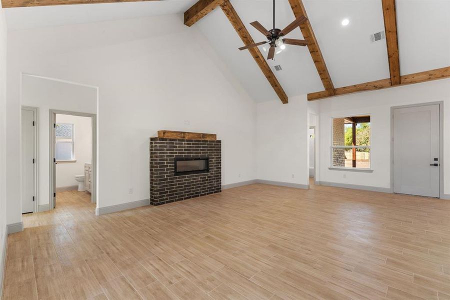 Unfurnished living room with high vaulted ceiling, a brick fireplace, light wood finished floors, beam ceiling, and ceiling fan
