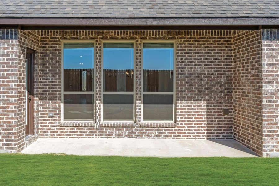 Brick home exterior with three large windows, concrete patio, and green lawn Brick home exterior with three large windows, concrete patio, and green lawn
