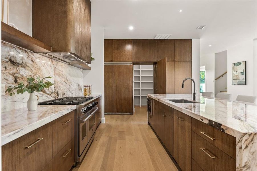 Kitchen with light stone countertops, double oven range, light wood finished floors, backsplash, and recessed lighting Kitchen with light stone countertops, double oven range, light wood finished floors, backsplash, and recessed lighting