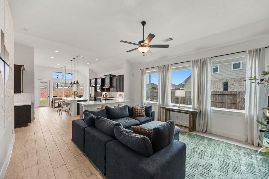 The open layout connects the living area to the kitchen and dining space, enhanced by recessed lighting and expansive windows overlooking the backyard.