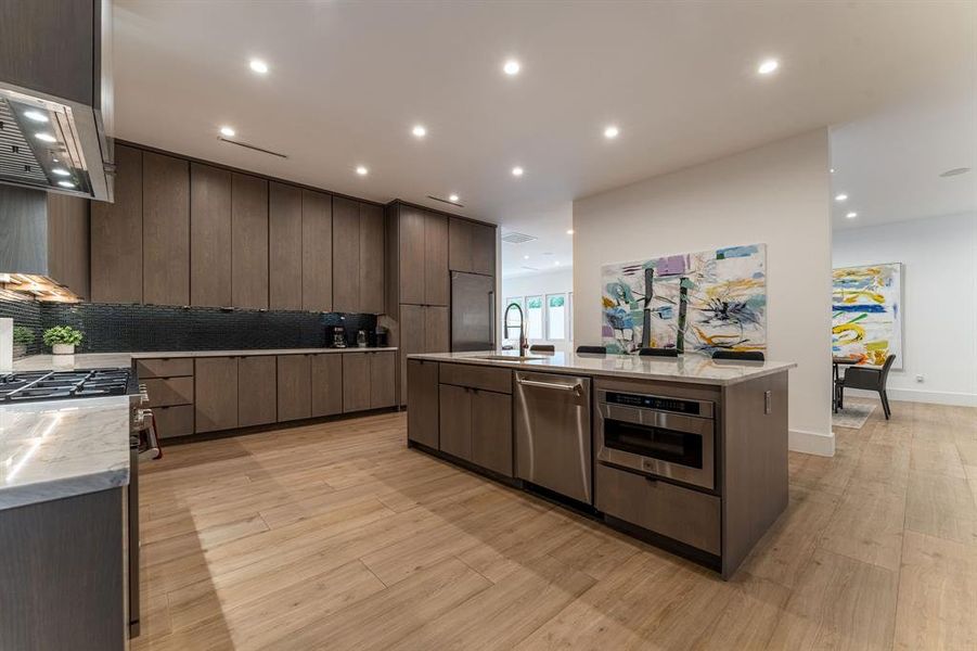 Kitchen with backsplash, light hardwood / wood-style floors, stainless steel appliances, and an island with sink Kitchen with backsplash, light hardwood / wood-style floors, stainless steel appliances, and an island with sink