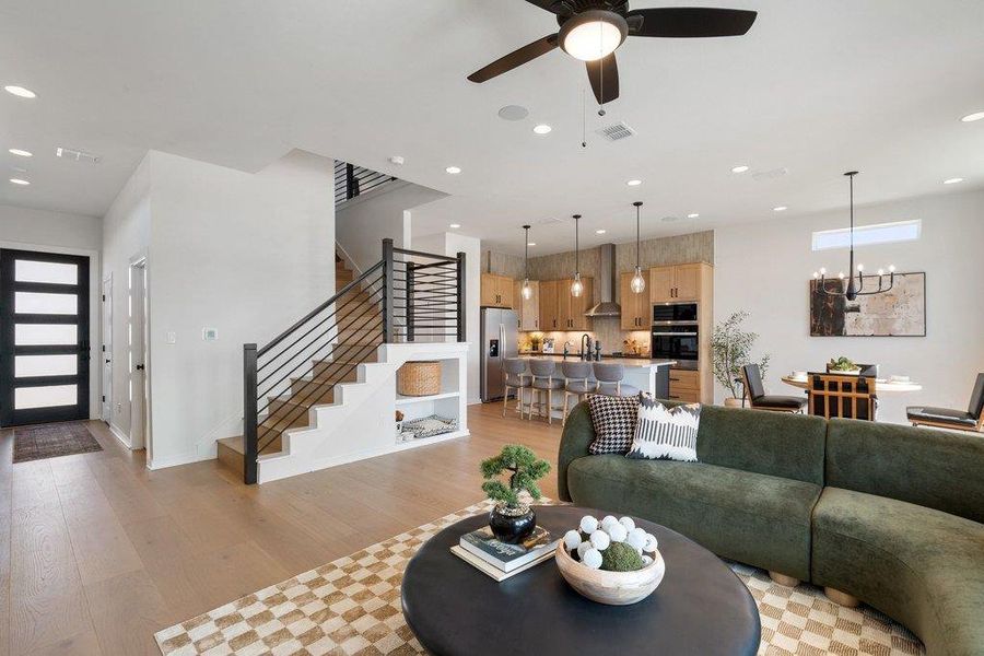 Open-concept living space featuring wood-finish flooring, a modern black railing staircase, recessed lighting, and a contemporary ceiling fan