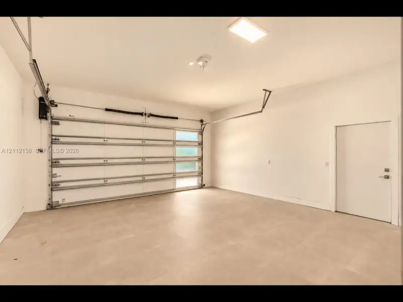 Finished garage with clean tile flooring, bright white walls, frosted-glass garage door for natural light, and direct interior access