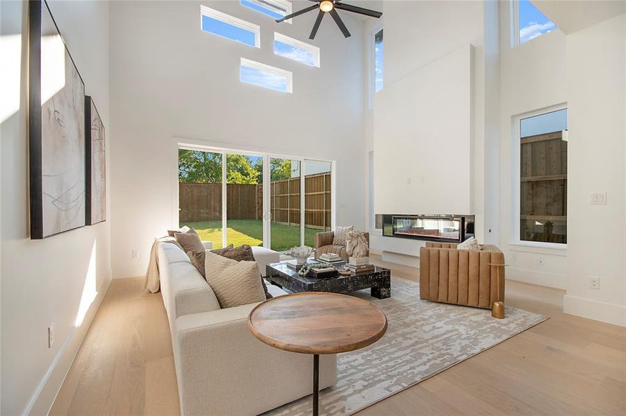 Living area featuring a glass covered fireplace, light wood finished floors, a high ceiling, and a ceiling fan Living area featuring a glass covered fireplace, light wood finished floors, a high ceiling, and a ceiling fan