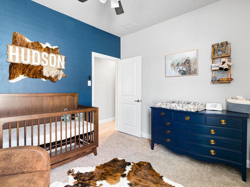 Carpeted bedroom featuring ceiling fan and a nursery area