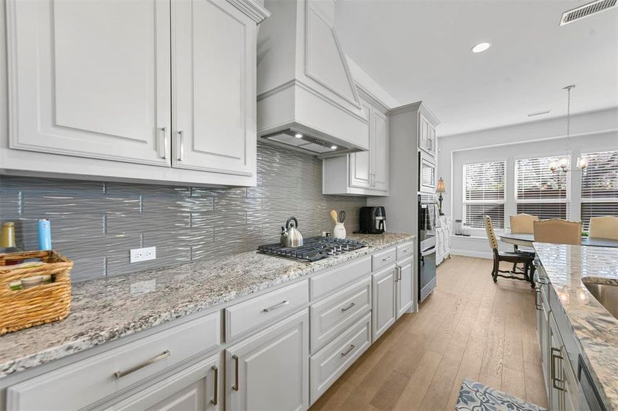 Kitchen with decorative light fixtures, premium range hood, stainless steel appliances, white cabinets, and a chandelier