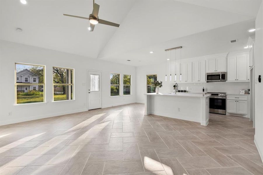 Kitchen with decorative light fixtures, white cabinetry, appliances with stainless steel finishes, high vaulted ceiling, and ceiling fan