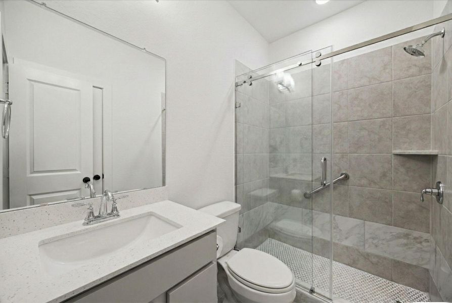 A SECONDARY BATHROOM INCLUDES A SINGLE VANITY WITH A STONE COUNTERTOP AND A GLASS-ENCLOSED SHOWER WITH TILE WALLS.