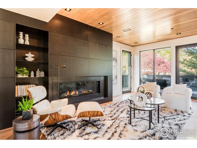 Among the many custom designer features in the home includes a stylish living area with blackened steel shelving and a wood paneled fireplace wall.