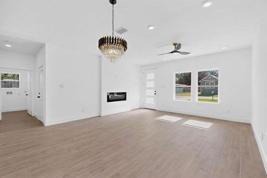 Unfurnished living room with light wood-type flooring, a chandelier, a glass covered fireplace, a ceiling fan, and recessed lighting