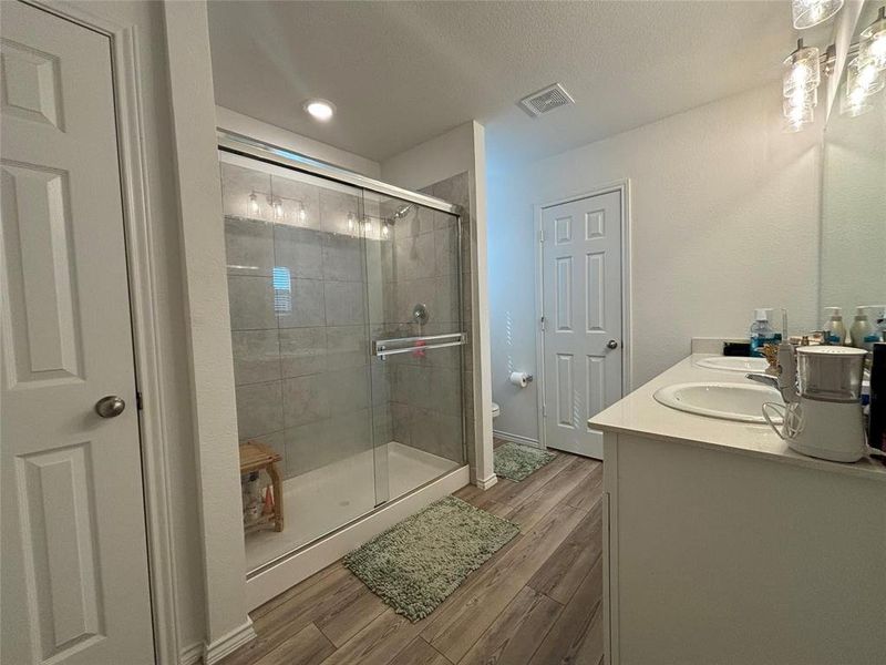 Full bath featuring a shower stall, wood finished floors, double vanity, and a textured ceiling
