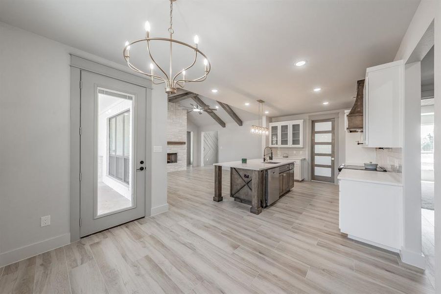 Kitchen featuring white cabinetry, a stone fireplace, decorative light fixtures, a chandelier, and glass insert cabinets