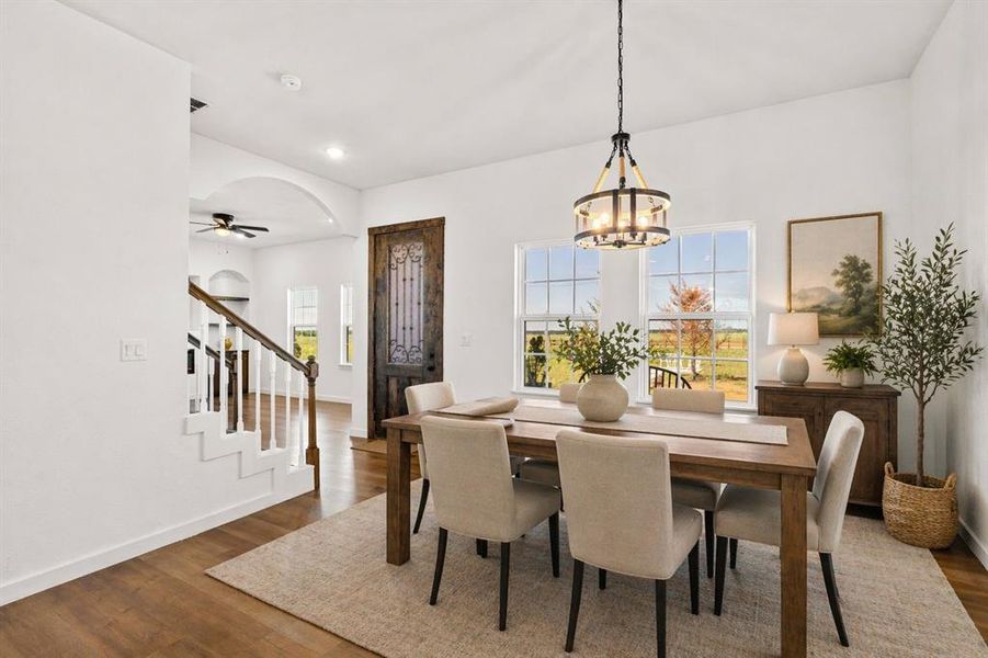 Bright dining area featuring wood-finish flooring, a contemporary chandelier, two large windows, a decorative dark wood door, and an arched entryway