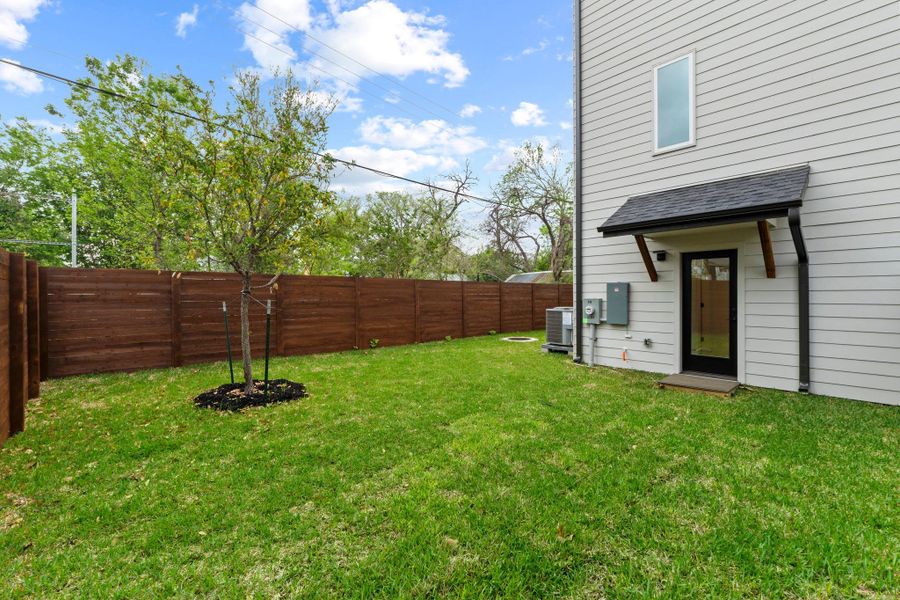 A wooden privacy fence surrounds the grassy backyard and features a sheltered secondary entrance.