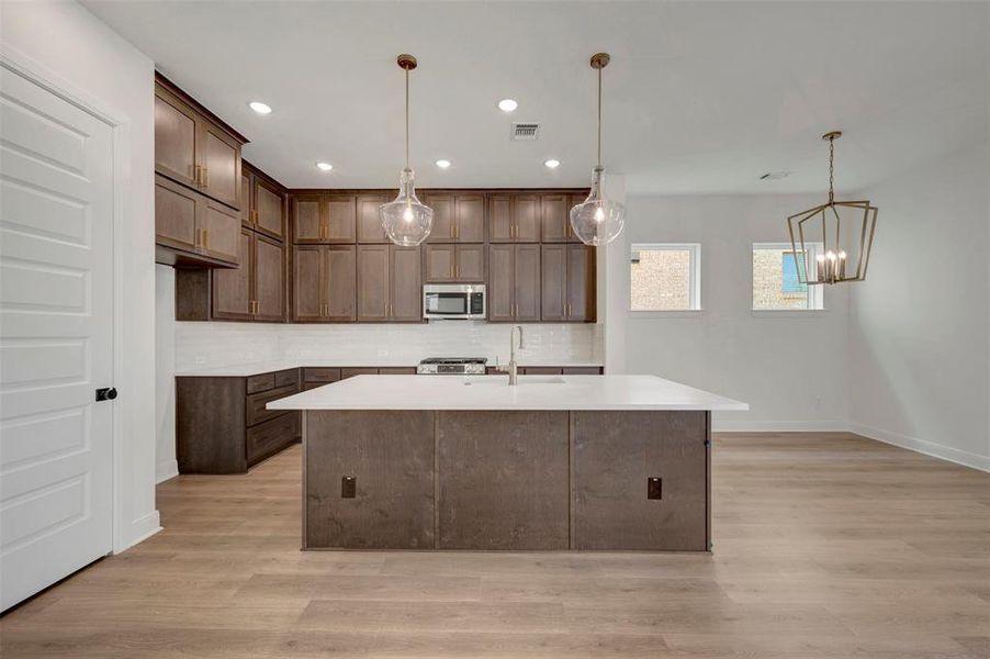 Modern kitchen featuring a large island with a light-toned countertop, dark wood-finish cabinetry, stainless steel appliances, and wood-finish flooring