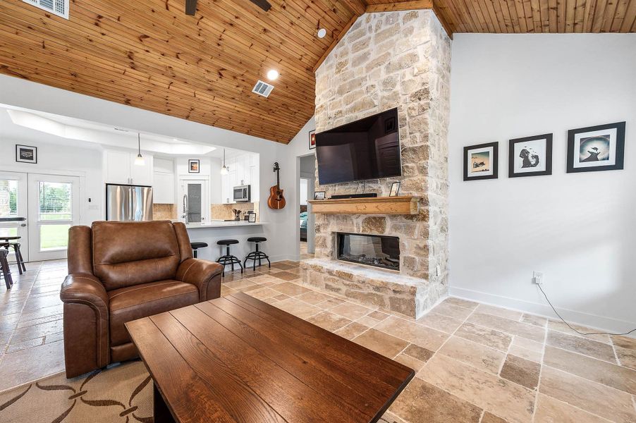 The open-concept design creates a seamless flow between the living area and kitchen, highlighted by soaring wood ceilings, a stunning stone fireplace, and bright natural light throughout. Modern finishes and functional design make this space ideal for both everyday living and entertaining.