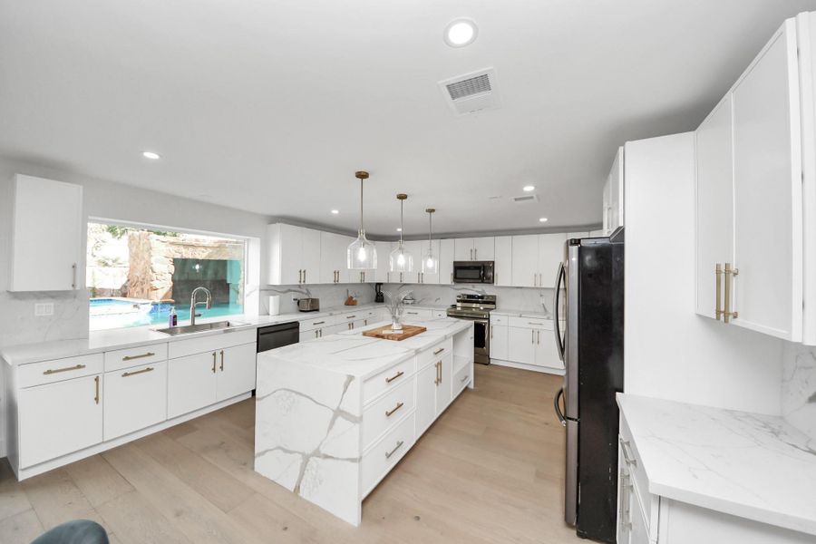 The modern kitchen features sleek white cabinetry complemented by gold hardware, quartz countertops and backsplash, a large island, and stainless-steel appliances. The modern kitchen features sleek white cabinetry complemented by gold hardware, quartz countertops and backsplash, a large island, and stainless-steel appliances.