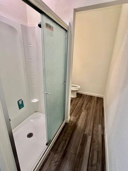 Bathroom with wood-type flooring, a shower with shower door, and toilet