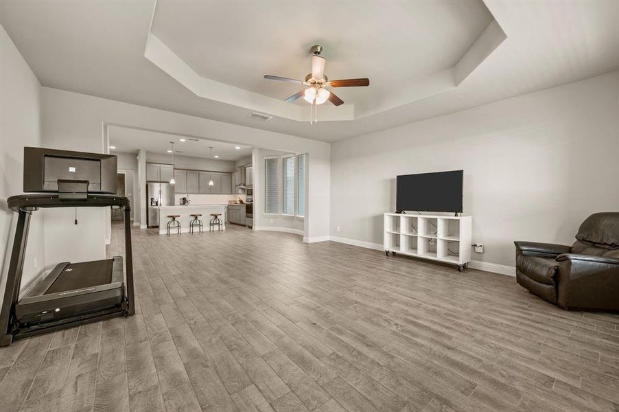 Expansive living room featuring a tray ceiling, ceiling fan, and plenty of space to design your perfect gathering area.