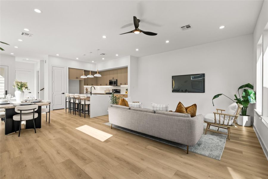 This view shows the depth and open layout of the main floor. The light oak flooring runs continuously from the living room windows, past the kitchen island, and right into the dining area, making the entire space easy to navigate and use.