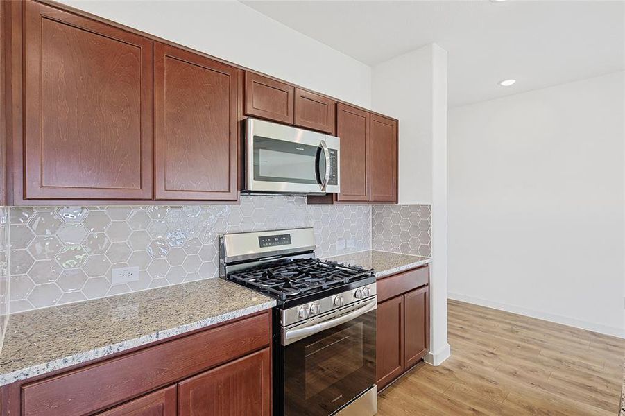 Kitchen with decorative backsplash, appliances with stainless steel finishes, light wood-type flooring, and light stone counters