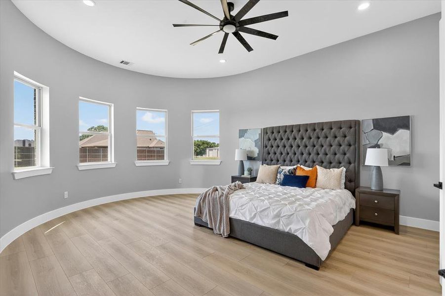 Spacious bedroom featuring light wood-finish flooring, a curved wall with four windows, and recessed lighting