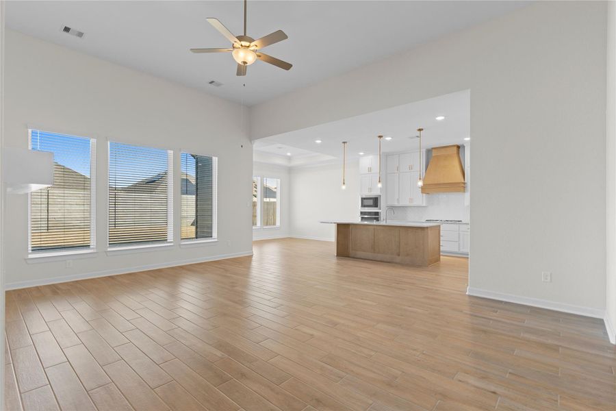 This wide view highlights the seamless open concept design, where the family room flows effortlessly into the kitchen and dining areas, all unified by continuous wood like tile flooring, offering both visual appeal and practical living for modern lifestyles.