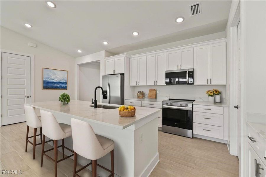 Kitchen with stainless steel appliances, a breakfast bar area, an island with sink, white cabinets, and light stone counters