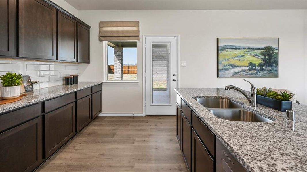 Kitchen featuring dark brown cabinets, light wood-style floors, light stone counters, and tasteful backsplash Kitchen featuring dark brown cabinets, light wood-style floors, light stone counters, and tasteful backsplash