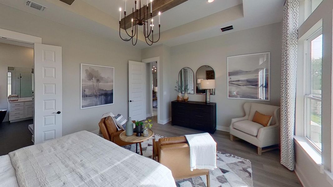 Bedroom with a raised ceiling, wood finished floors, a chandelier, and connected bathroom
