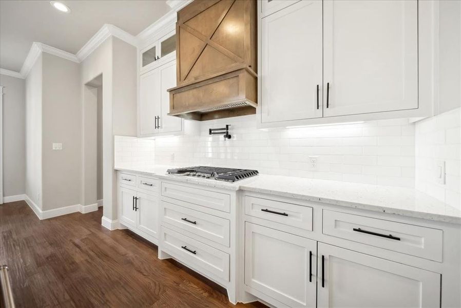 Kitchen featuring stainless steel gas cooktop, ornamental molding, white cabinets, light stone countertops, and backsplash