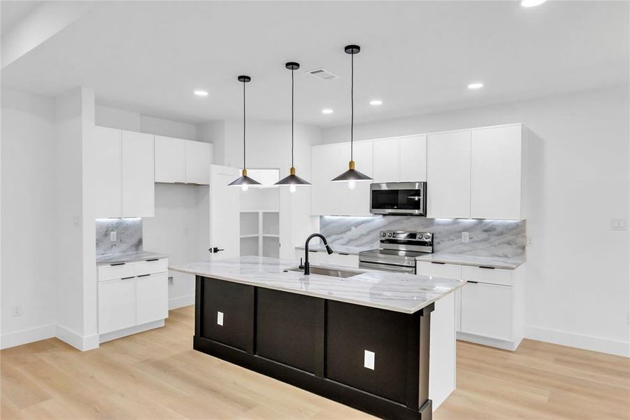Kitchen with decorative backsplash, light stone counters, white cabinetry, appliances with stainless steel finishes, and decorative light fixtures