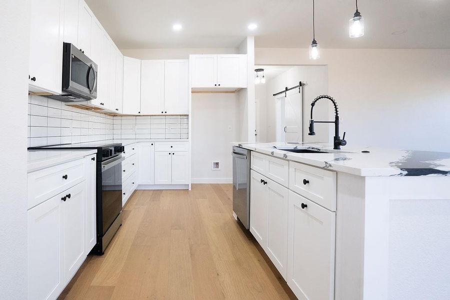Kitchen featuring stainless steel appliances, a barn door, white cabinetry, pendant lighting, and recessed lighting