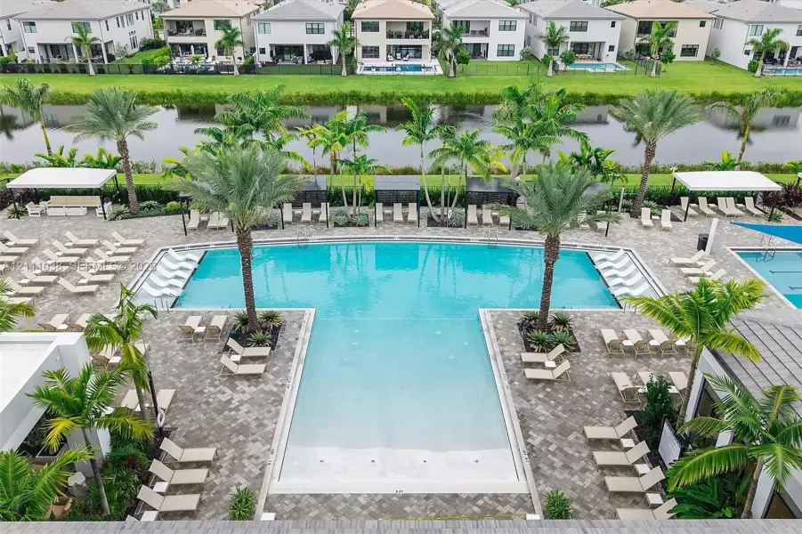 Community pool featuring a shallow sun shelf, paver surround, mature palm trees, and covered cabanas