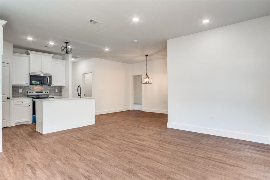 Kitchen with white cabinets, decorative backsplash, light wood-style floors, appliances with stainless steel finishes, and recessed lighting