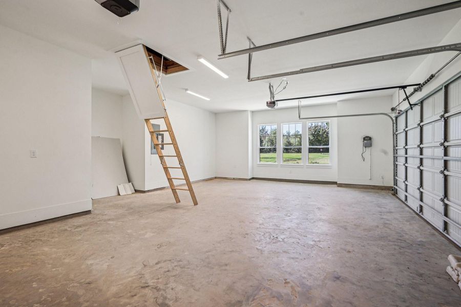 This spacious garage features a clean concrete floor, a large window for natural light, and an attic access with a pull-down ladder. The garage door is modern and automated, providing convenience and functionality. Perfect for storage or parking.