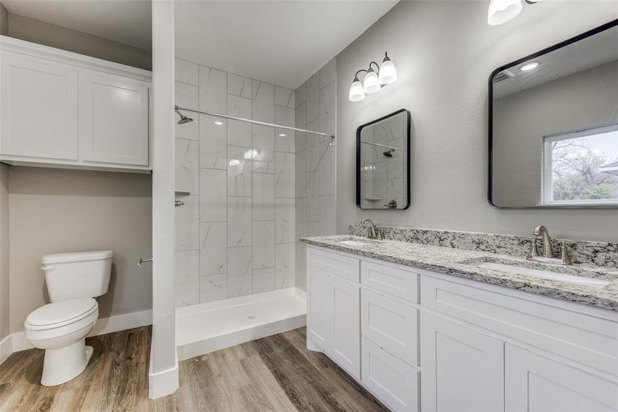 Bathroom featuring a marble finish shower, double vanity, and light wood-style floors