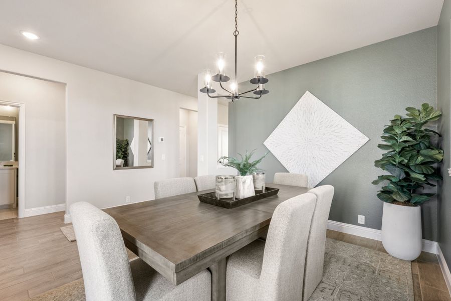 Dining room with wood table, upholstered chairs, chandelier, and gray-green accent wall with hardwood floors