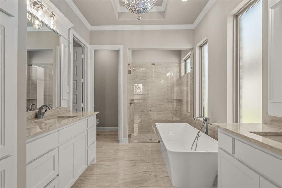 Bathroom with two vanities, a stall shower, a soaking tub, crown molding, and light marble finish floors