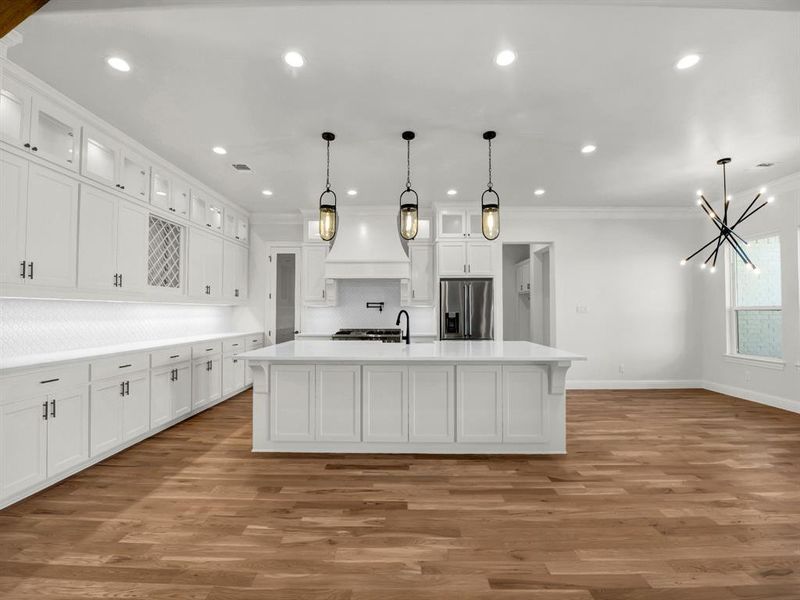 Kitchen with stainless steel fridge with ice dispenser, crown molding, decorative light fixtures, a kitchen island with sink, and white cabinets